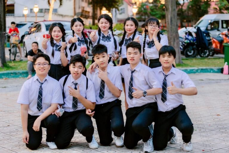 Cheerful group of students in uniform posing with thumbs up outdoors.